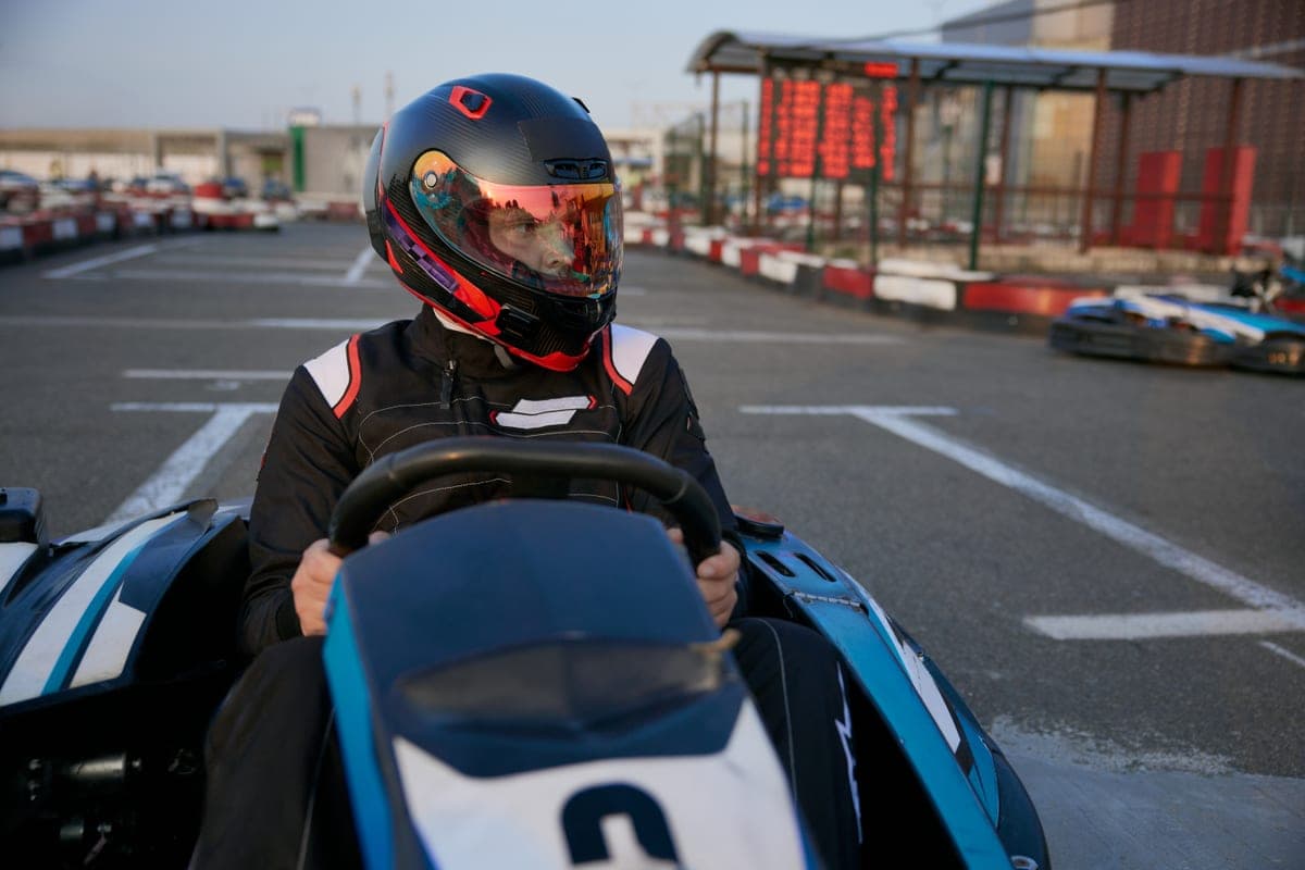 Řidič v helmě a kombinéze na motokáře na venkovní dráze