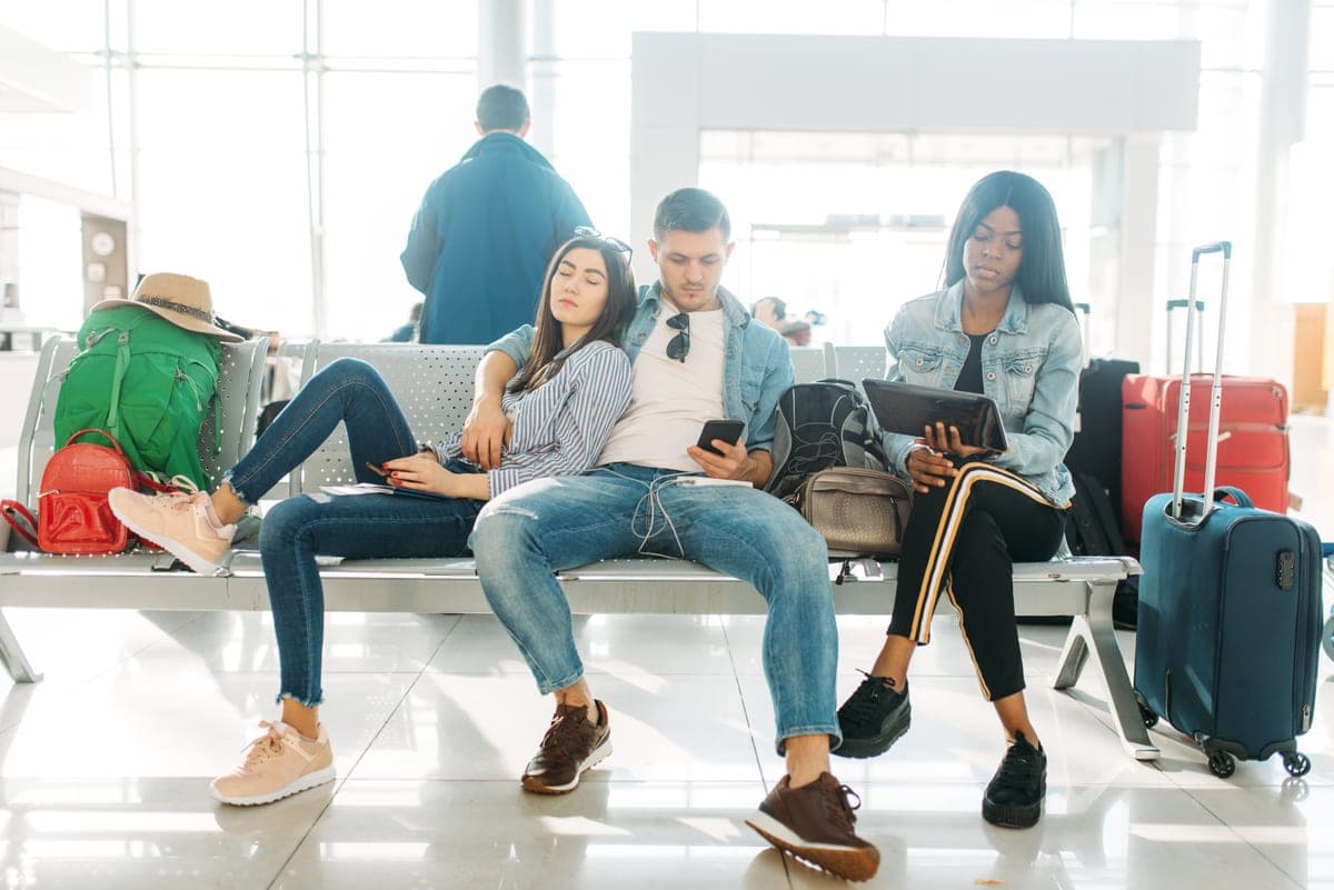 Cestující s kufry a batohy čekají na lavici v odletové hale