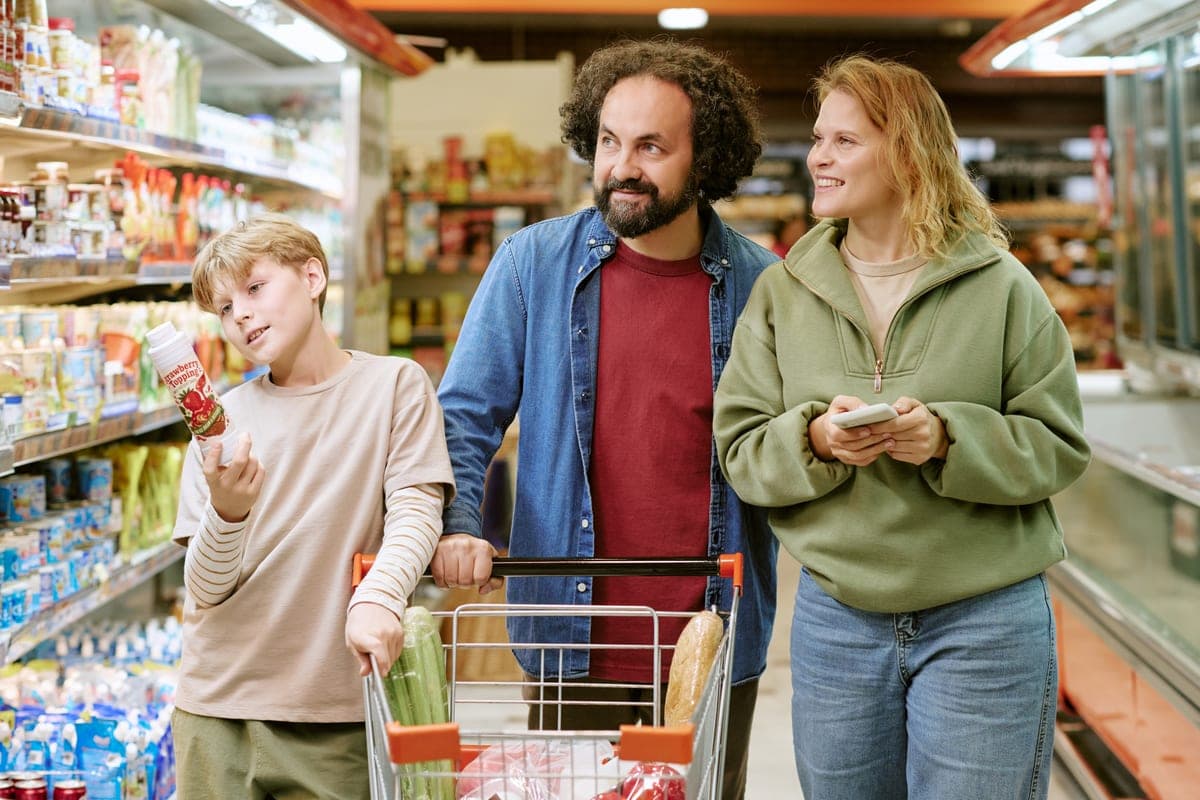 Rodina s nákupním vozíkem v supermarketu, žena drží v ruce telefon